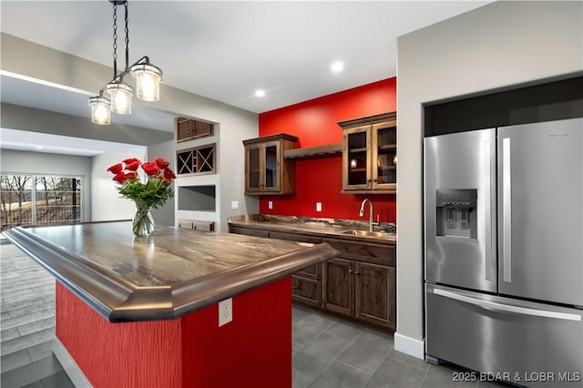 kitchen with dark countertops, a kitchen island, glass insert cabinets, stainless steel fridge with ice dispenser, and a sink