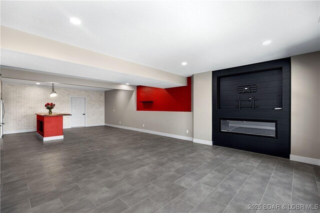 unfurnished living room with recessed lighting, a large fireplace, baseboards, and brick wall