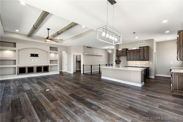 kitchen with a kitchen island with sink, a ceiling fan, open floor plan, arched walkways, and dark brown cabinetry