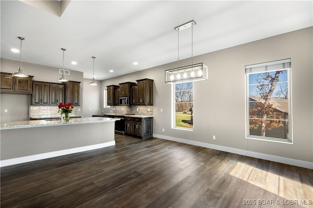 kitchen with dark brown cabinetry, stainless steel microwave, dark wood-style floors, and decorative backsplash