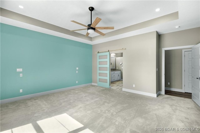 unfurnished bedroom featuring carpet, baseboards, ensuite bathroom, a barn door, and a raised ceiling