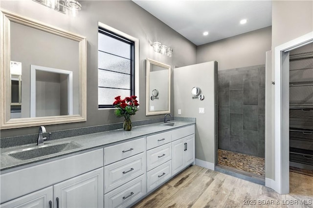 full bathroom featuring double vanity, wood finished floors, a walk in shower, and a sink