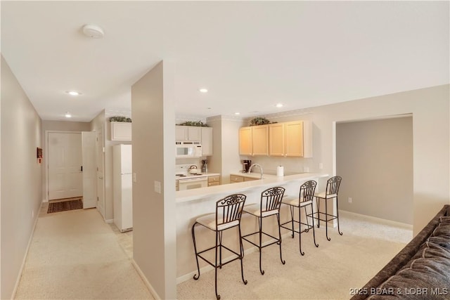 kitchen with light carpet, white appliances, baseboards, a breakfast bar, and a sink