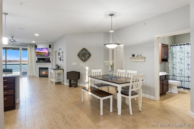 dining area featuring light wood-type flooring, a fireplace, baseboards, and a ceiling fan