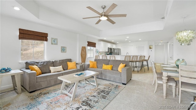 living room with recessed lighting, a raised ceiling, light carpet, and ceiling fan with notable chandelier