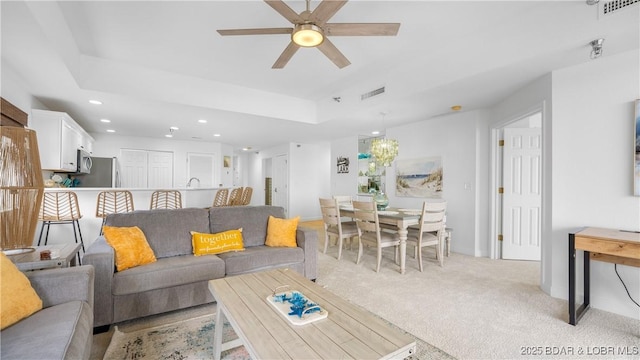 living area with light carpet, a raised ceiling, visible vents, and recessed lighting