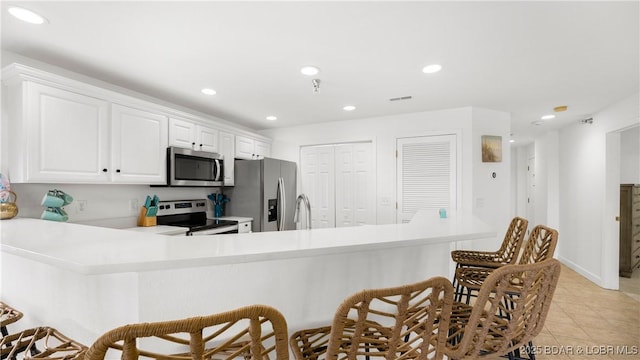 kitchen featuring white cabinets, appliances with stainless steel finishes, a kitchen breakfast bar, light countertops, and recessed lighting