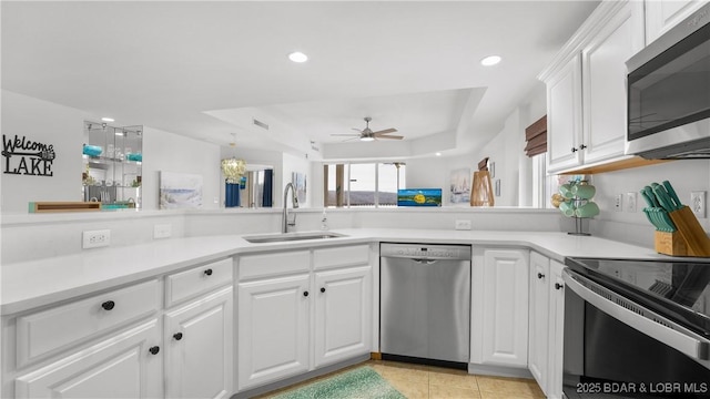 kitchen with white cabinets, a raised ceiling, light countertops, stainless steel appliances, and a sink