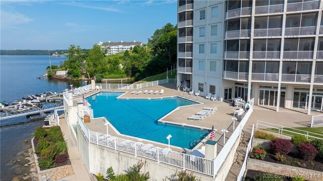 pool with a patio area, fence, and a water view