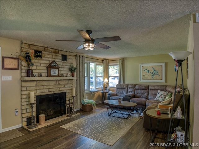 living room with baseboards, a ceiling fan, wood finished floors, a textured ceiling, and a stone fireplace