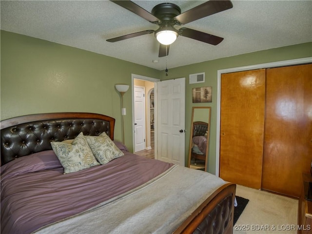 bedroom featuring light carpet, visible vents, ceiling fan, a textured ceiling, and a closet