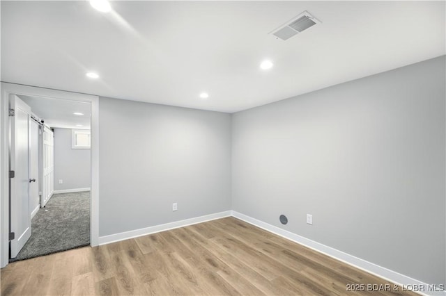 spare room featuring light wood-type flooring, visible vents, recessed lighting, a barn door, and baseboards