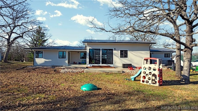 rear view of property with a sunroom, a lawn, and a playground