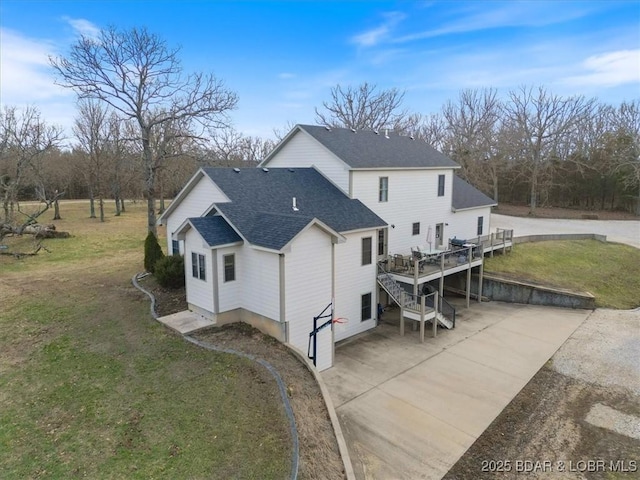 back of property with roof with shingles, a lawn, a deck, and stairs