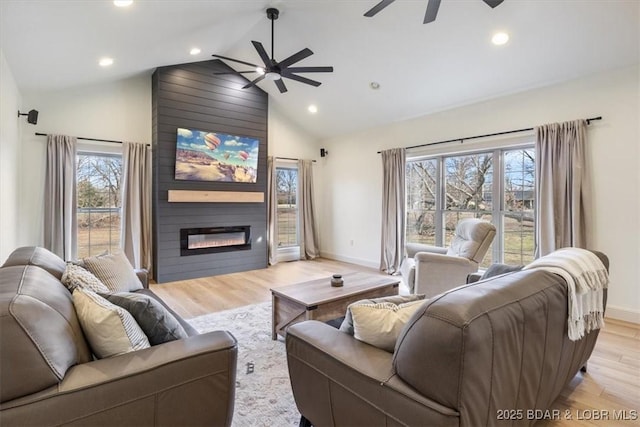 living area featuring a large fireplace, baseboards, light wood-style flooring, and a ceiling fan