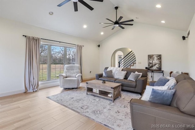 living area featuring ceiling fan, high vaulted ceiling, arched walkways, light wood-style flooring, and stairs