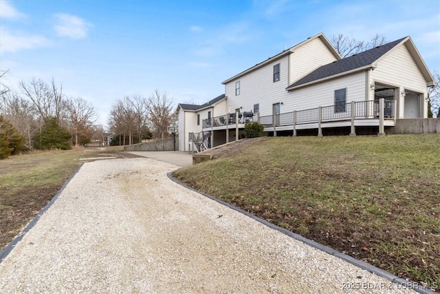 view of side of home with driveway, a garage, a lawn, and a wooden deck