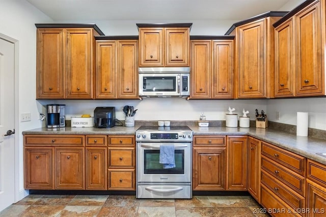 kitchen featuring dark countertops, brown cabinetry, stone finish floor, and stainless steel appliances