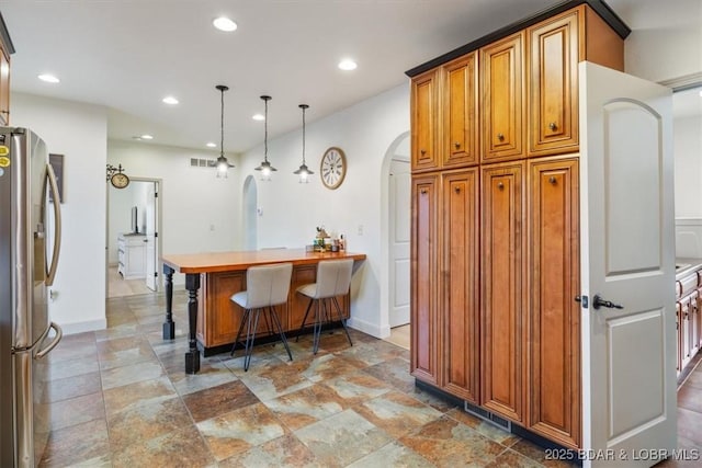 kitchen featuring arched walkways, brown cabinets, decorative light fixtures, recessed lighting, and stainless steel fridge with ice dispenser