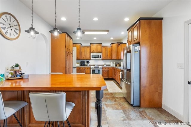 kitchen featuring arched walkways, a peninsula, a kitchen breakfast bar, appliances with stainless steel finishes, and brown cabinetry