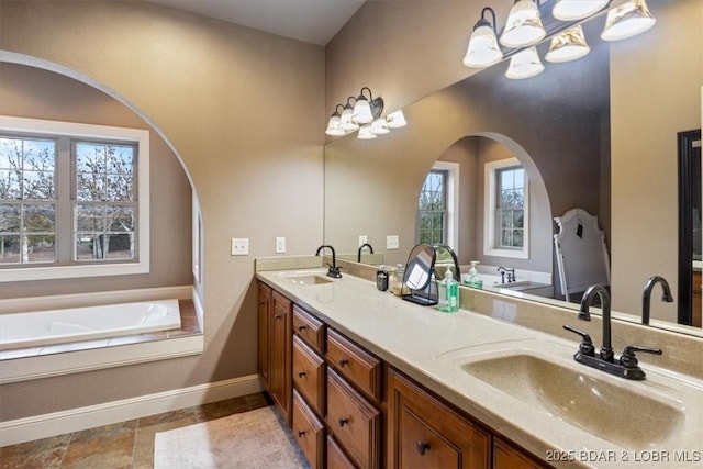 bathroom featuring baseboards, a sink, a bath, and double vanity