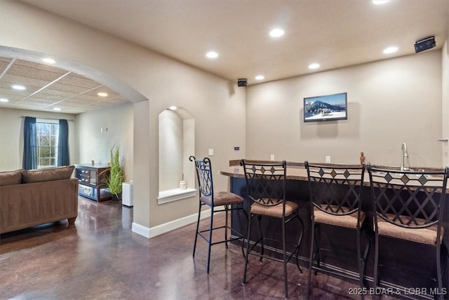 bar featuring arched walkways, recessed lighting, finished concrete floors, bar area, and baseboards