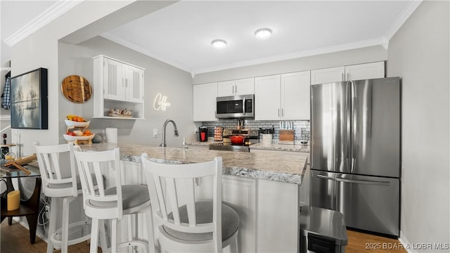 kitchen with ornamental molding, tasteful backsplash, stainless steel appliances, a breakfast bar area, and white cabinets