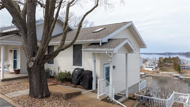 view of front of house featuring a water view, roof with shingles, central AC unit, and entry steps