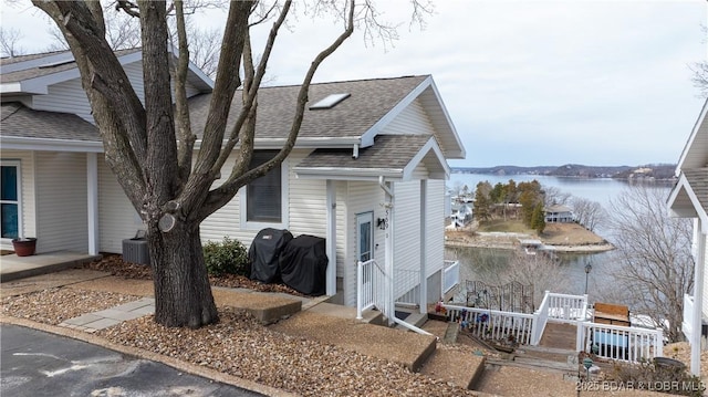 view of front facade featuring central AC unit, entry steps, roof with shingles, and a water view