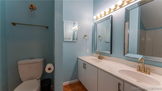 bathroom featuring double vanity, a sink, toilet, and wood finished floors