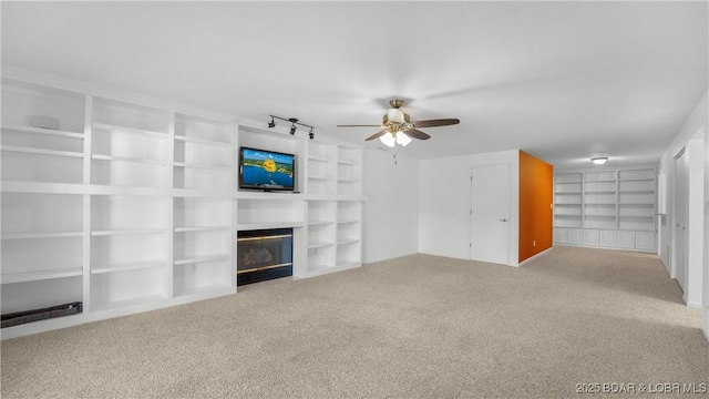 unfurnished living room with a fireplace with flush hearth, carpet flooring, ceiling fan, and built in shelves