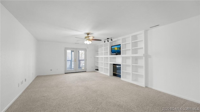 unfurnished living room with a ceiling fan, baseboards, french doors, carpet, and a glass covered fireplace