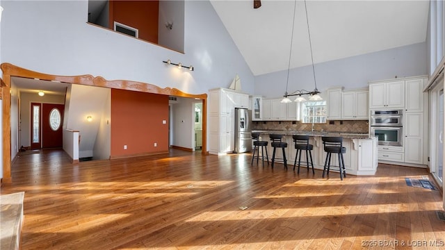 kitchen featuring high vaulted ceiling, stainless steel appliances, white cabinets, a kitchen breakfast bar, and tasteful backsplash