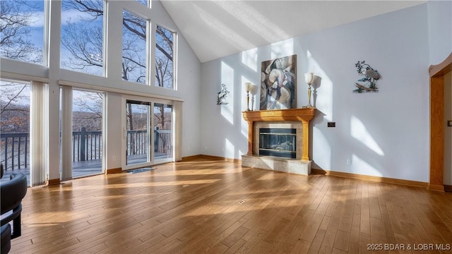 unfurnished living room with baseboards, wood-type flooring, high vaulted ceiling, and a tiled fireplace