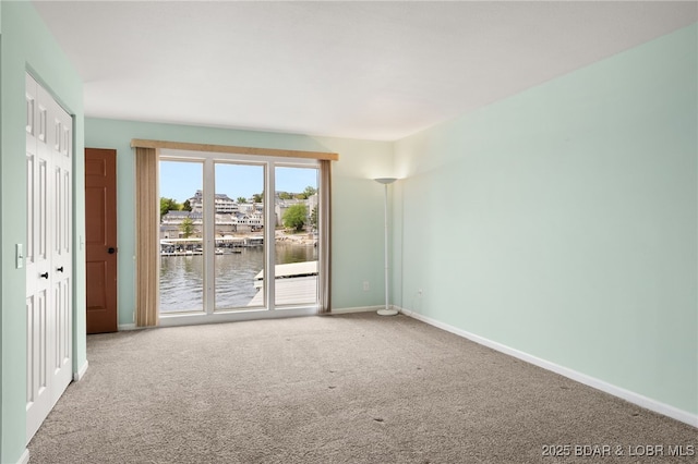 carpeted empty room featuring a water view and baseboards