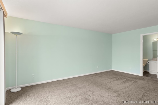 unfurnished bedroom with dark colored carpet, baseboards, and ensuite bathroom