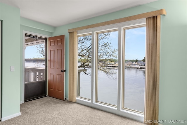entryway with baseboards, a water view, a healthy amount of sunlight, and light carpet