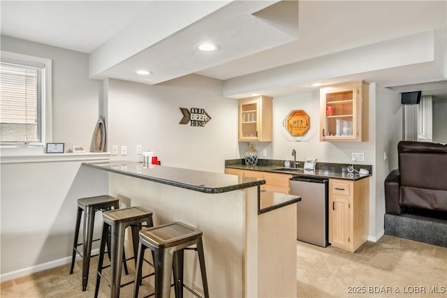 kitchen featuring dishwasher, light brown cabinetry, dark countertops, and a sink