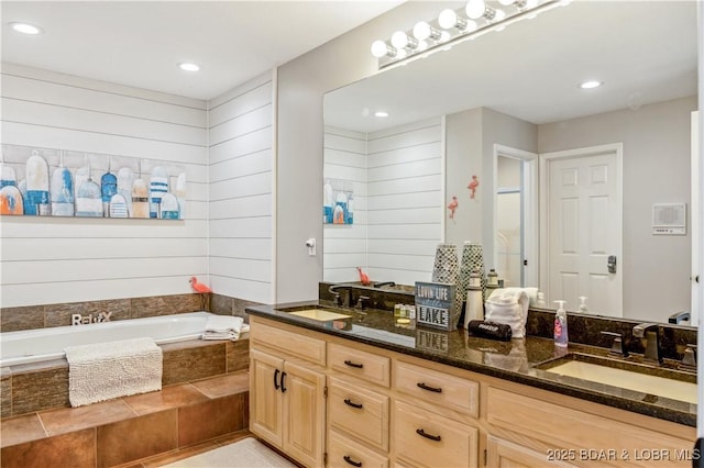 bathroom with double vanity, a sink, a bath, and recessed lighting