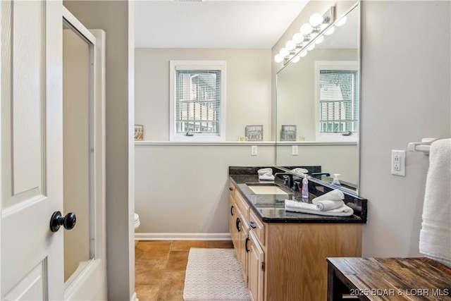 bathroom featuring a shower, toilet, vanity, and baseboards