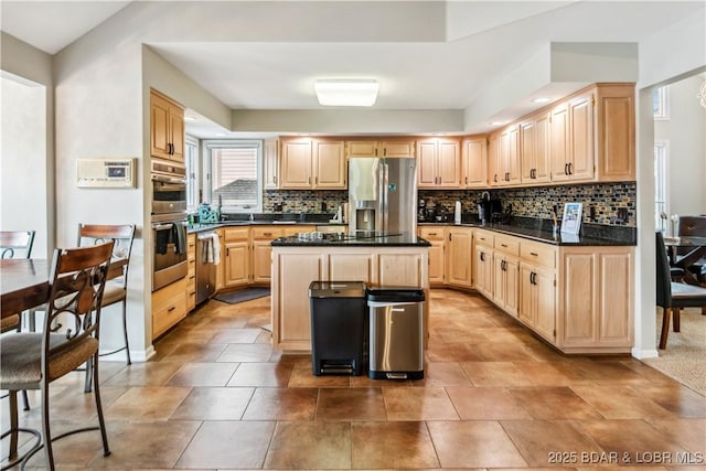 kitchen with light brown cabinets, appliances with stainless steel finishes, dark countertops, backsplash, and a center island