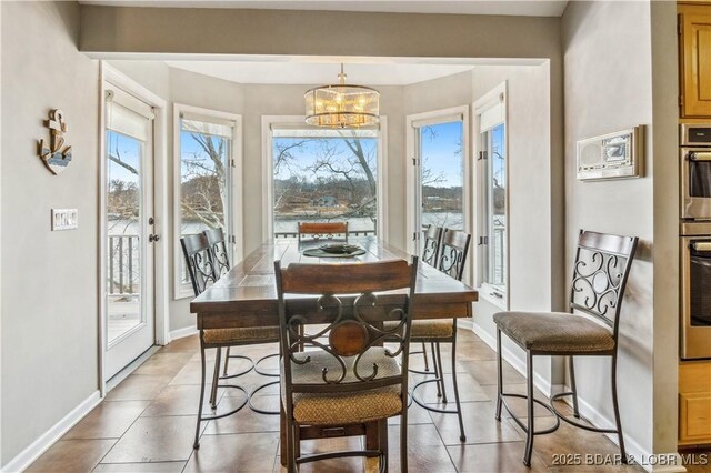 dining room featuring light tile patterned flooring, a healthy amount of sunlight, baseboards, and an inviting chandelier