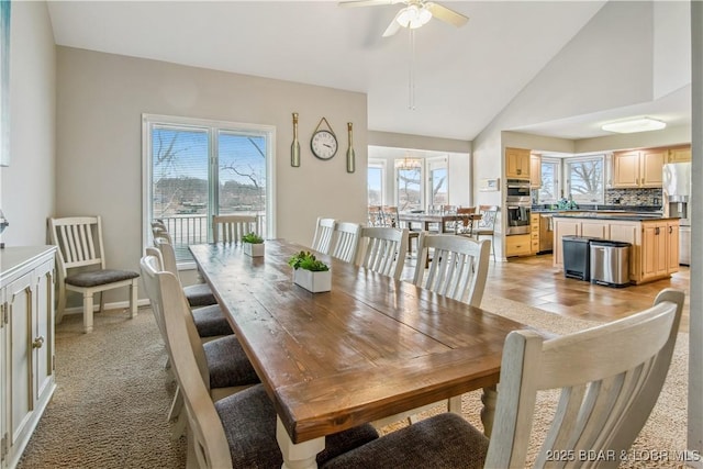 dining room featuring light carpet, high vaulted ceiling, and a ceiling fan