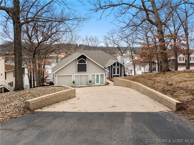 view of front of house featuring a chimney, a shingled roof, a garage, a residential view, and driveway