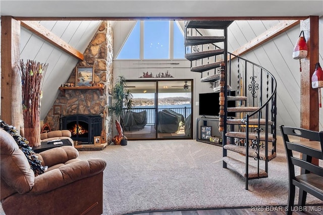 living room featuring high vaulted ceiling, a stone fireplace, wooden walls, carpet flooring, and stairway