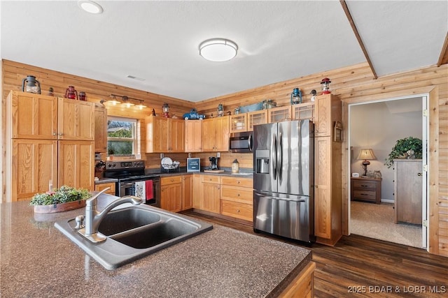 kitchen featuring dark countertops, dark wood-style floors, appliances with stainless steel finishes, wood walls, and a sink