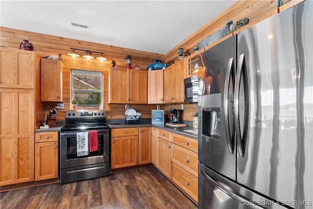 kitchen featuring dark wood-style flooring, stainless steel appliances, dark countertops, visible vents, and wooden walls