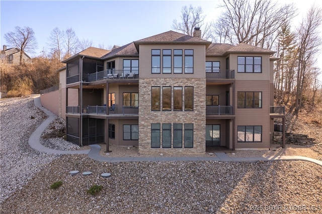 back of house featuring stone siding, a chimney, a balcony, and a sunroom