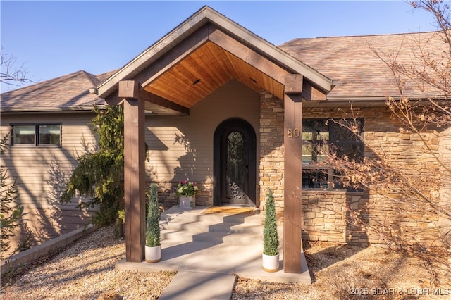 entrance to property with stone siding and a shingled roof