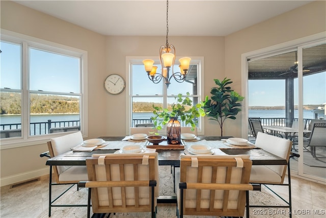 dining area with a notable chandelier, visible vents, a water view, and baseboards